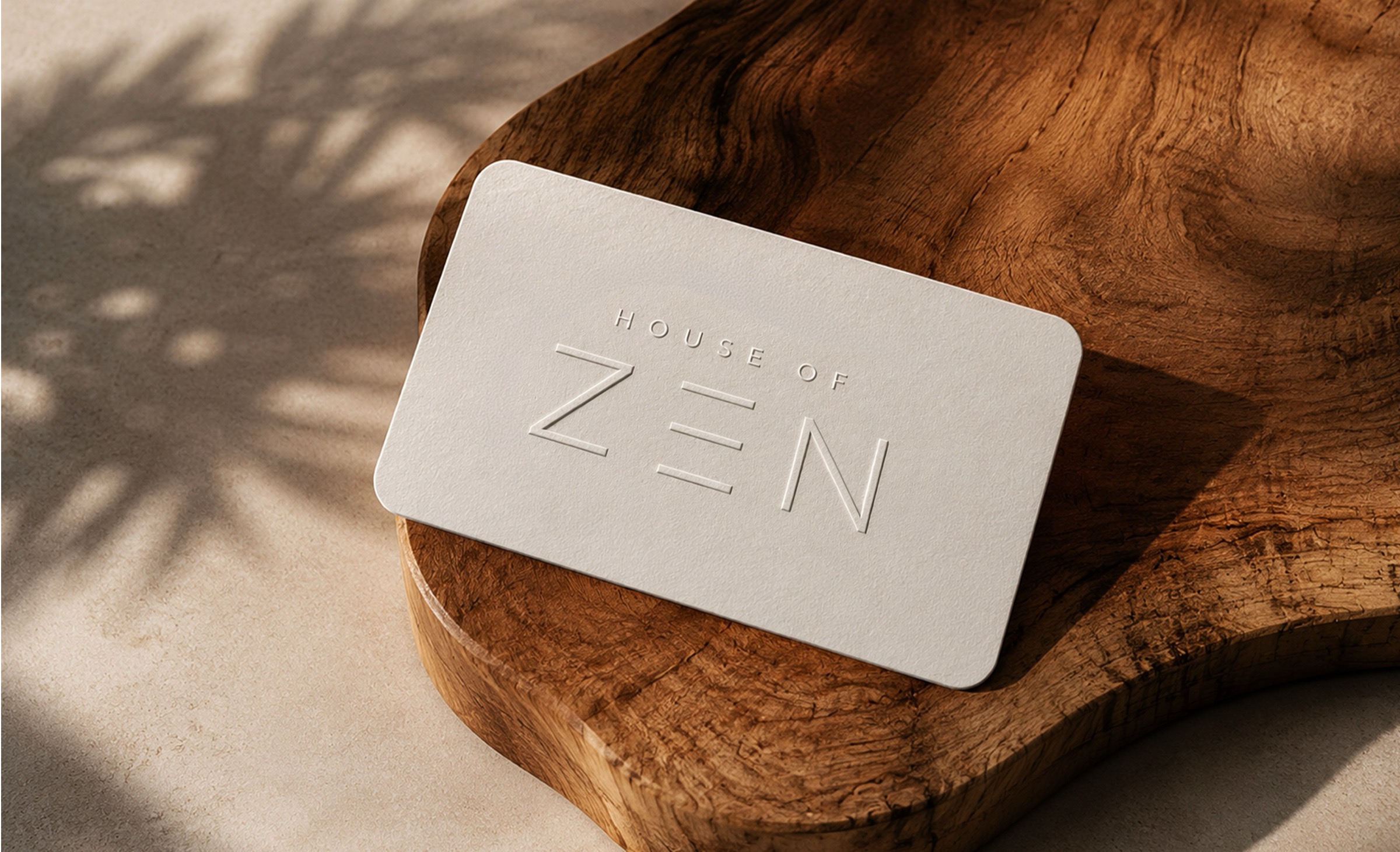 The House of Zen identity, blind-embossed on soft cotton card, resting on a hand-carved walnut form.